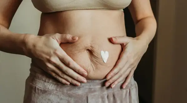 Kobieta z kremem w kształcie serca na brzuchu, szukająca domowych sposobów na obkurczanie macicy.