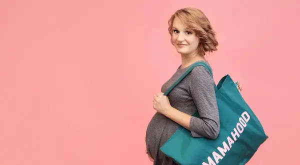 Przyszła mama z torbą "Mamahood" na ramieniu, gotowa do porodu.