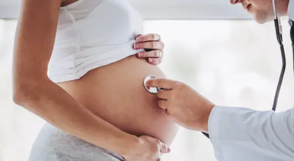 Lekarz osłuchuje brzuch kobiety w 24 tygodniu ciąży. Słychać bicie serca dziecka.