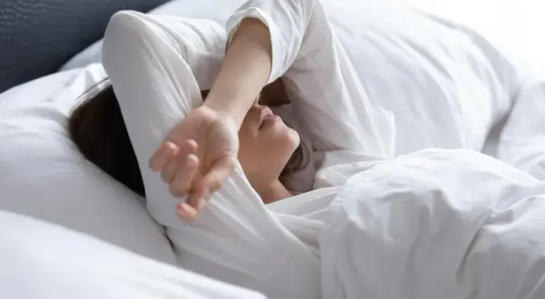 Kobieta w białej pościeli, z ręką na czole, doświadcza bezsenności w ciąży.