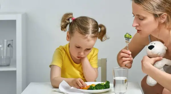 Mama zachęca dziecko do jedzenia brokułów. Trudna dieta dwulatka, ale mama się nie poddaje.