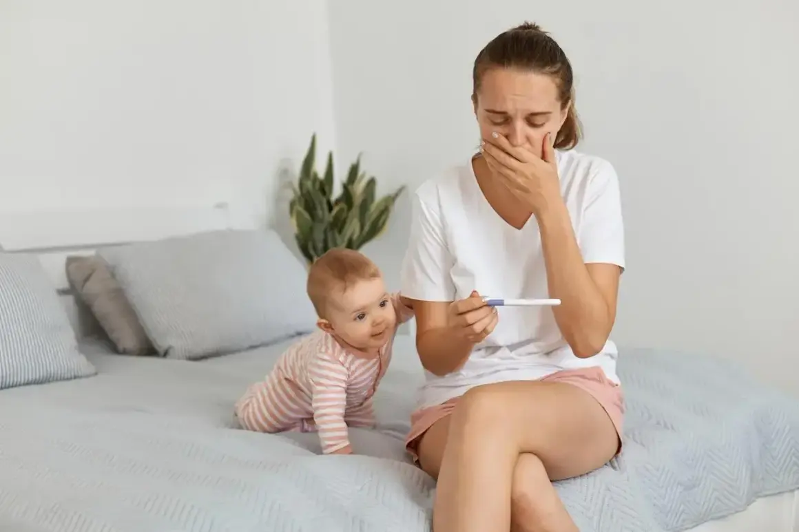 Zaskoczona mama z niemowlakiem na rękach trzyma test ciążowy. Zastanawia się, po jakim czasie można zajść w ciążę po porodzie naturalnym.