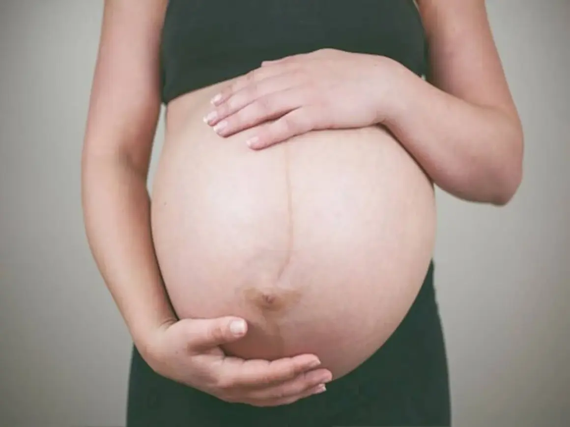 Brzuch kobiety w ciąży, dłonie delikatnie go obejmują. To czas, gdy czuć już wyraźne ruchy dziecka w 27 tygodniu ciąży.