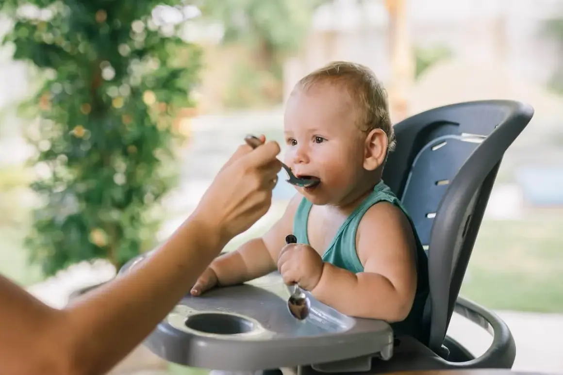 Maluch w krzesełku do karmienia z zaciekawieniem przyjmuje pierwszy posiłek. To ważny moment, kiedy rozszerzać dietę dziecka karmionego piersią.