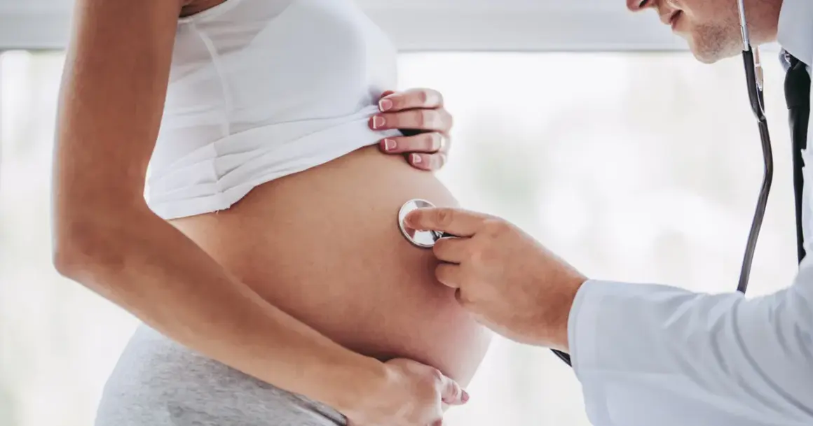 Lekarz osłuchuje brzuch kobiety w 24 tygodniu ciąży. Słychać bicie serca dziecka.