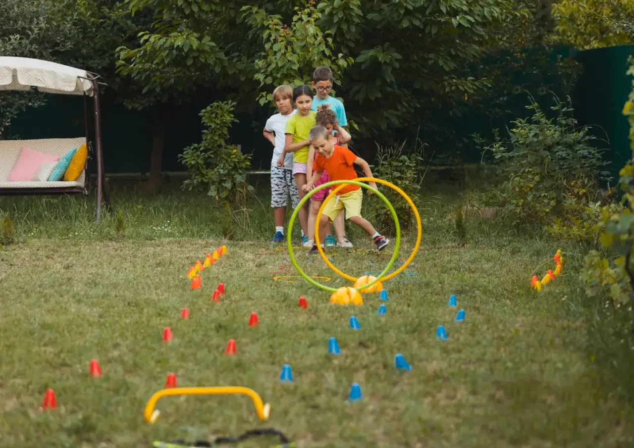 Dzieci bawią się w ogrodzie, pokonując tor przeszkód. Czy to dobra zabawa dla dzieci, jak w Stumble Guys?