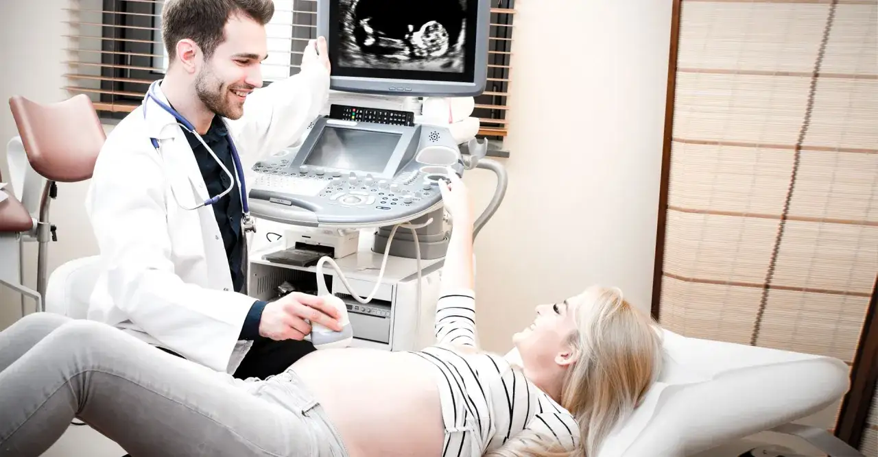 Lekarz wykonuje usg ciąży. Uśmiechnięta pacjentka leży na kozetce, a na monitorze widać obraz płodu.