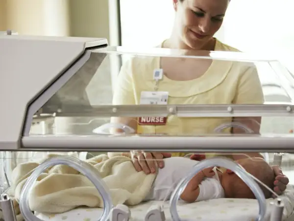 Pielęgniarka czule dotyka noworodka w inkubatorze. Dziecko urodziło się w 32. tygodniu ciąży, wymaga szczególnej opieki.
