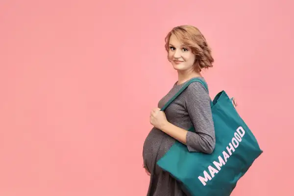 Przyszła mama z torbą "Mamahood" na ramieniu, gotowa do porodu.